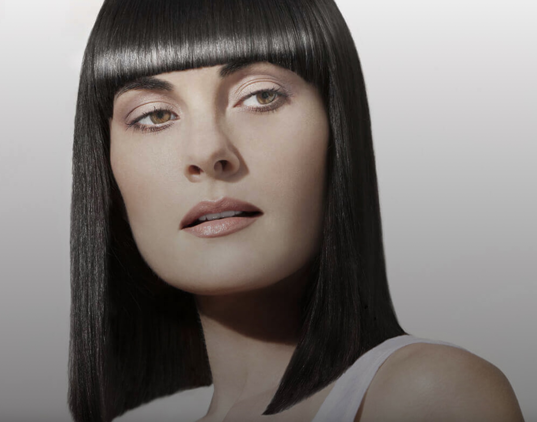 A woman with sleek, straight black hair and bangs, wearing a white top, looking to the side.